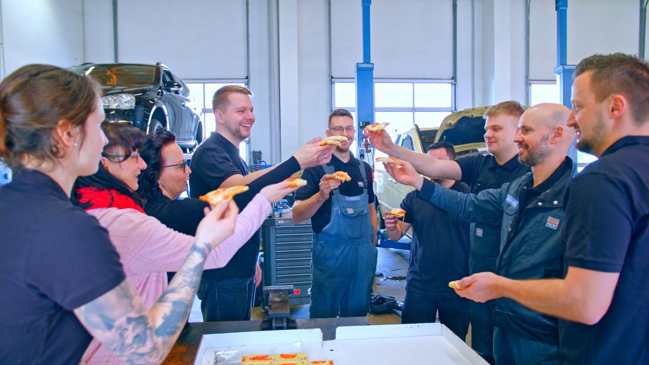 Team von Heil Automobile teilt sich in geselliger Runde eine Pizza in der Werkstatt in Leipzig